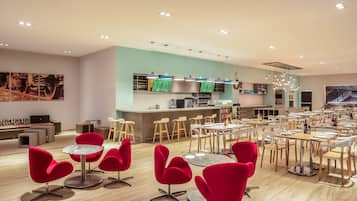 A modern restaurant with red chairs and tables, a kitchen area, and artwork on the walls.
