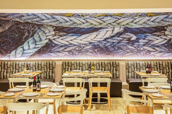 A restaurant with tables set for dining, chairs, and a large decorative wall.