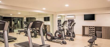A modern gym with treadmills, elliptical machines, and a bench.