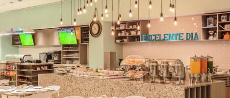 Un espace dédié au petit-déjeuner, aménagé avec un buffet proposant notamment un coin café, une sélection de fruits et des tables et chaises.