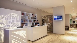 Un área de recepción moderna de hotel con un mostrador de recepción, una pantalla de televisión y una pared decorativa con patrones geométricos.