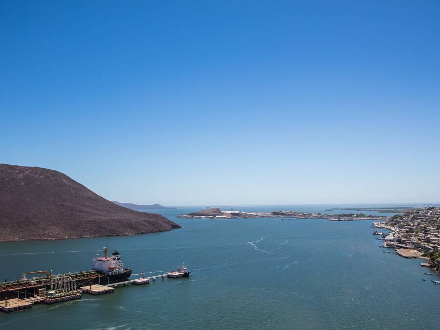 Una località costiera con una grande nave ormeggiata al molo, circondata da acqua e colline.