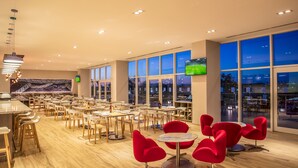 Un restaurante espacioso con múltiples mesas y sillas, ventanas amplias y una pantalla de televisión.