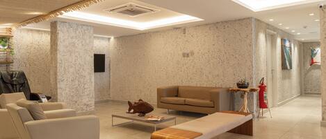 A modern lobby with a sofa, a wooden bench, a coffee table, and a fire extinguisher.
