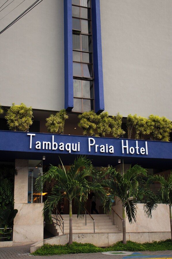 Exterior del hotel Tambaqui Praia con un letrero azul, palmeras y una escalera que conduce a la entrada.