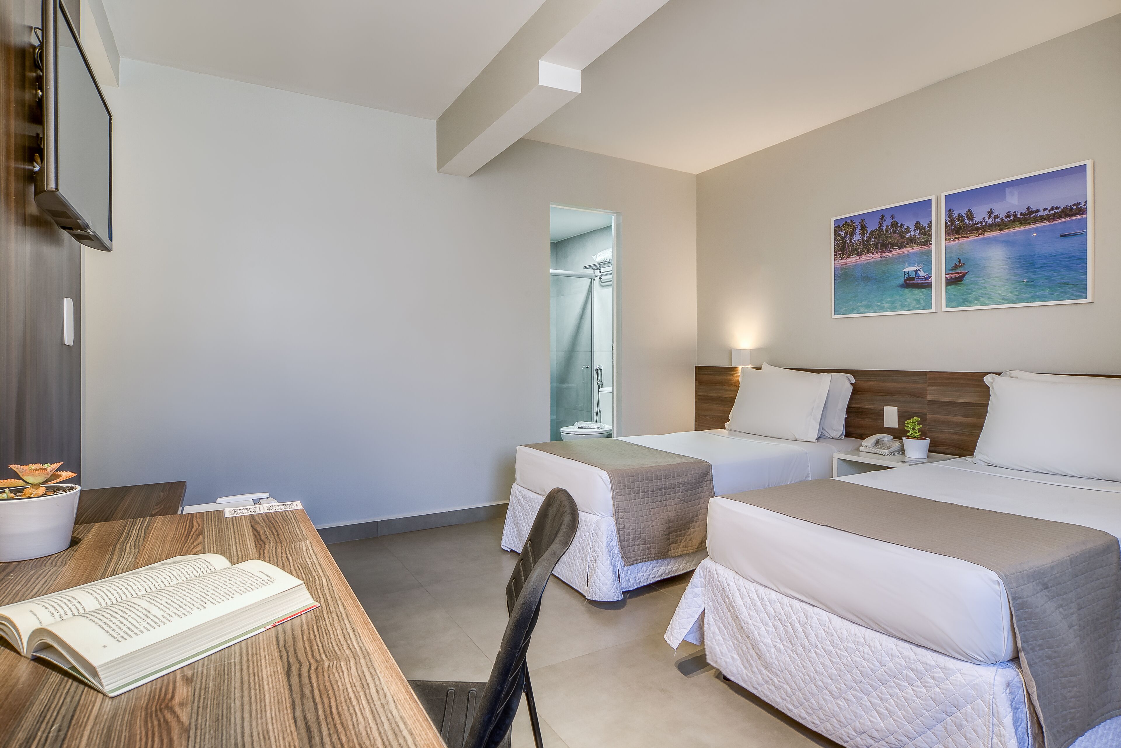 A hotel room with two beds, a desk with a book, a TV, and a shower.