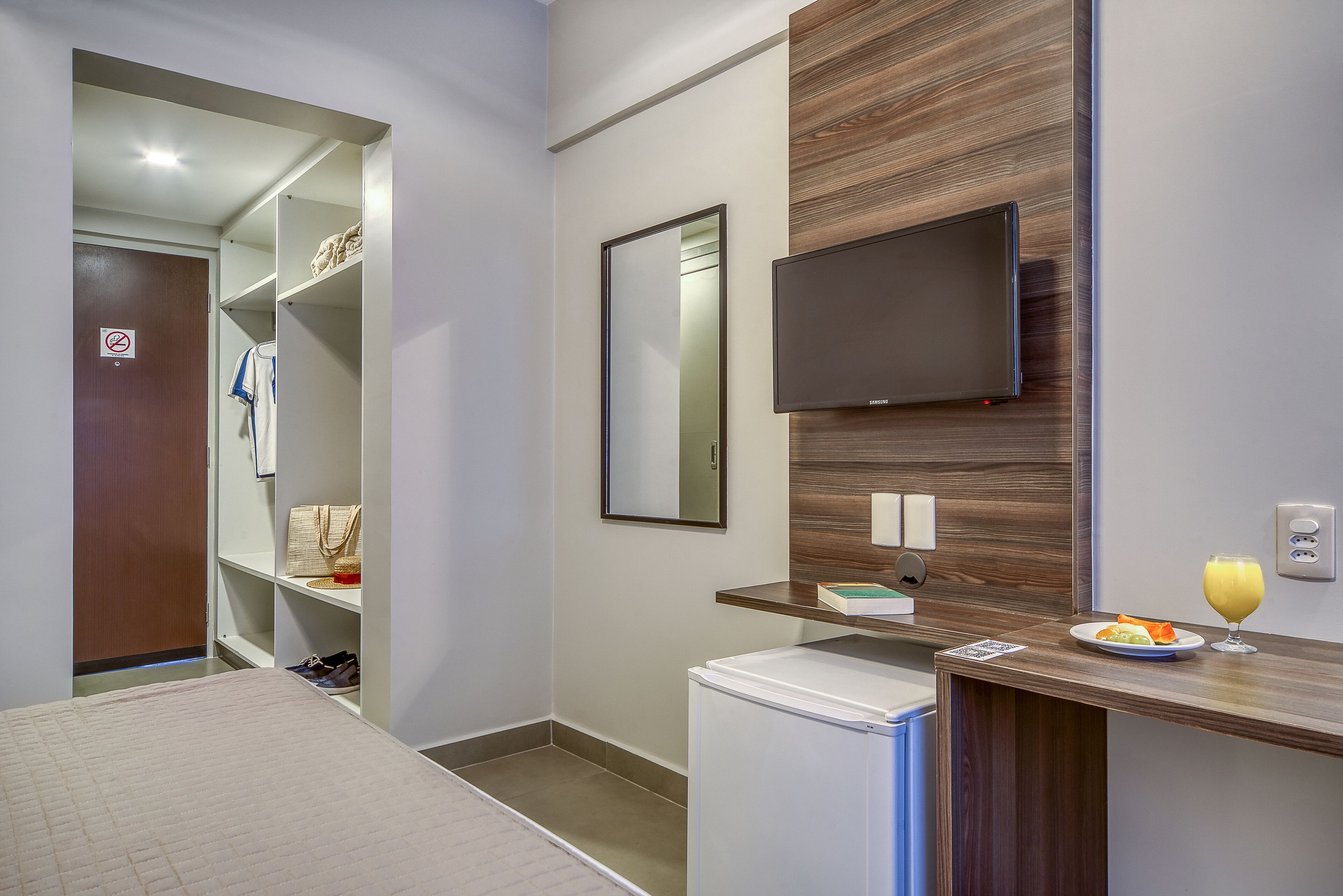 Un baño moderno con ducha, inodoro, lavamanos, espejo, televisión y un refrigerador pequeño.