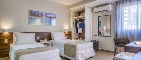 A hotel room with two beds, a desk, a chair, a wardrobe, and a bathroom.