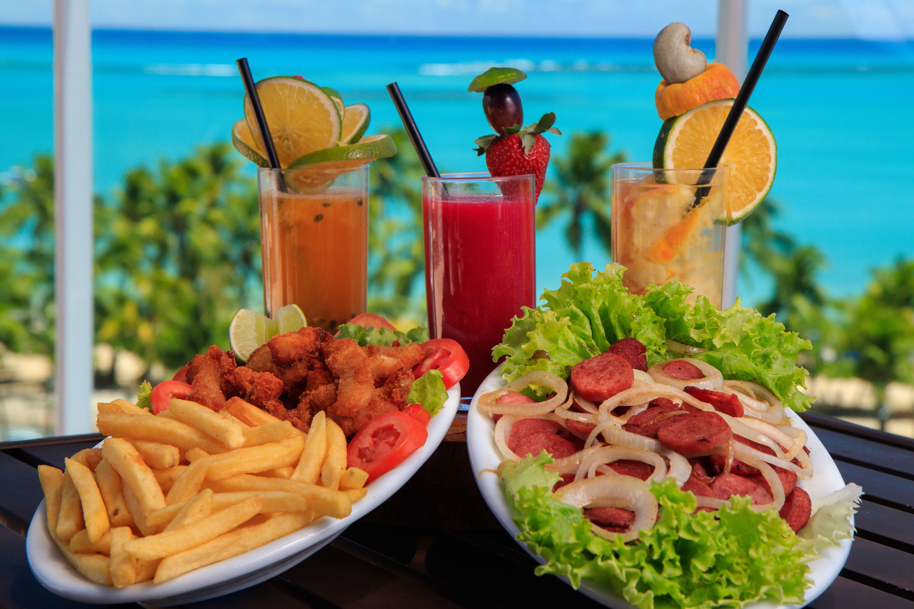Two plates of food with drinks on a table with a view of the ocean.