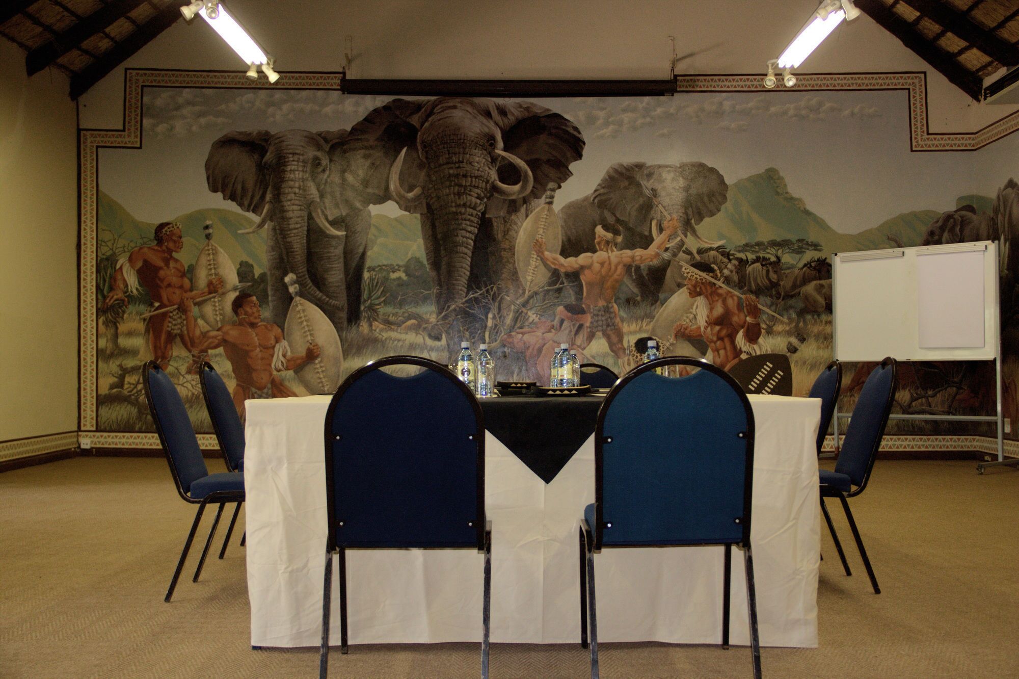 Un salón de conferencias con un mural de un elefante y un hombre, una pizarra y una mesa con sillas.