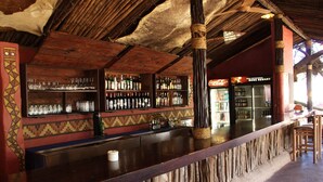 A bar area with wooden shelves stocked with bottles and glasses, a Coca-Cola refrigerator, and a sign indicating a reward program. - aha Shakaland (Eshowe)