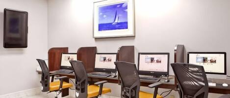 A conference room with four desks, each with a computer, chairs, and a framed picture on the wall.