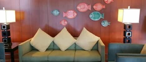 A room with a sofa, two lamps, and a wall with fish decorations.