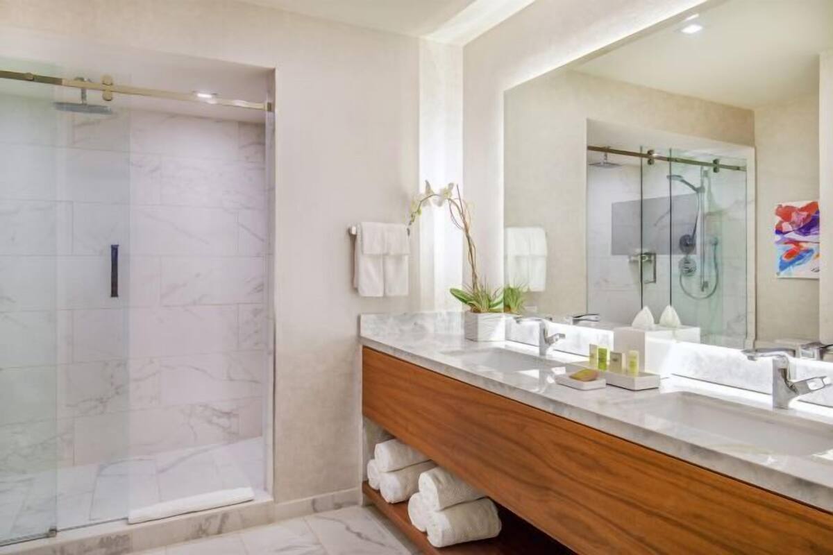A modern bathroom with a glass shower, marble tiles, a wooden vanity, and a large mirror.