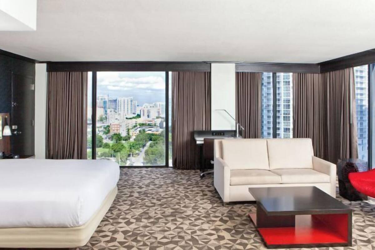 A hotel room with a bed, a sofa, a coffee table, and a desk.