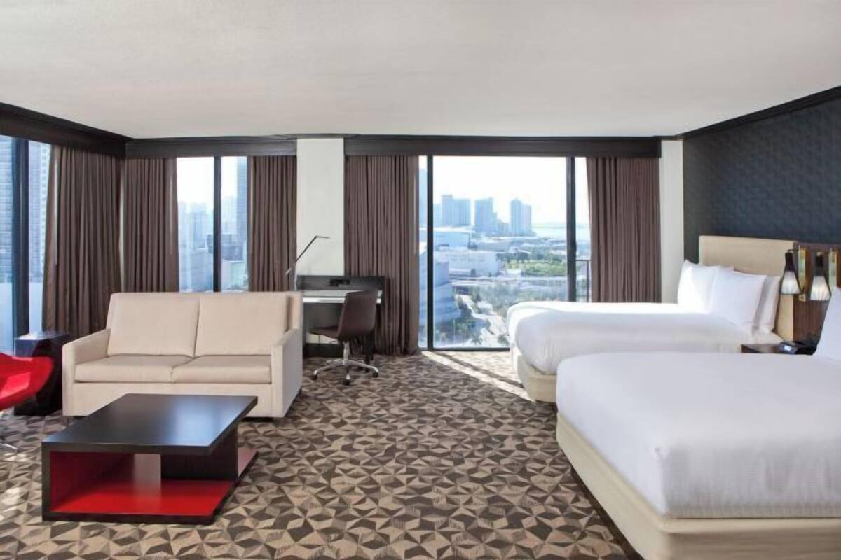 A hotel room with a city view, a sofa, a desk, and two beds.