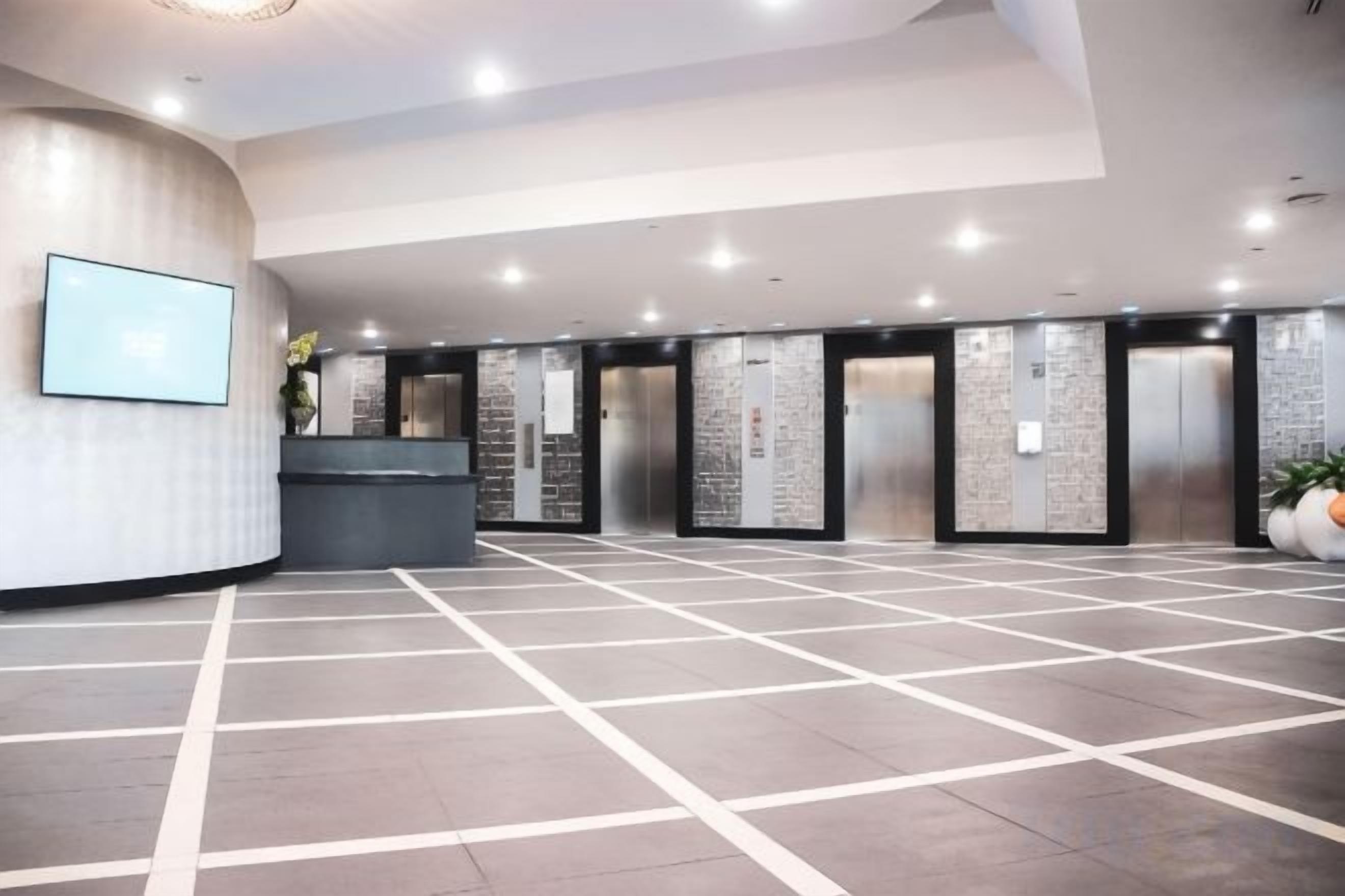 A hotel lobby with a reception desk, elevators, and a tiled floor.