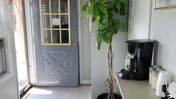 A modern interior with a grey door, a clock, a potted plant, a coffee machine, and stacked cups. - Dollar Inn (Somerset)