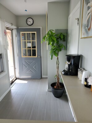 A modern interior with a grey door, a clock, a potted plant, a coffee machine, and stacked cups.