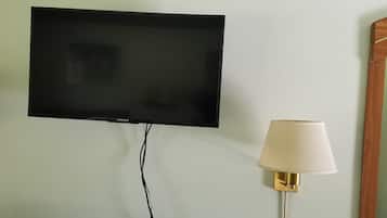 Un téléviseur à écran plat fixé au mur, une lampe de chevet et une table de chevet en bois.