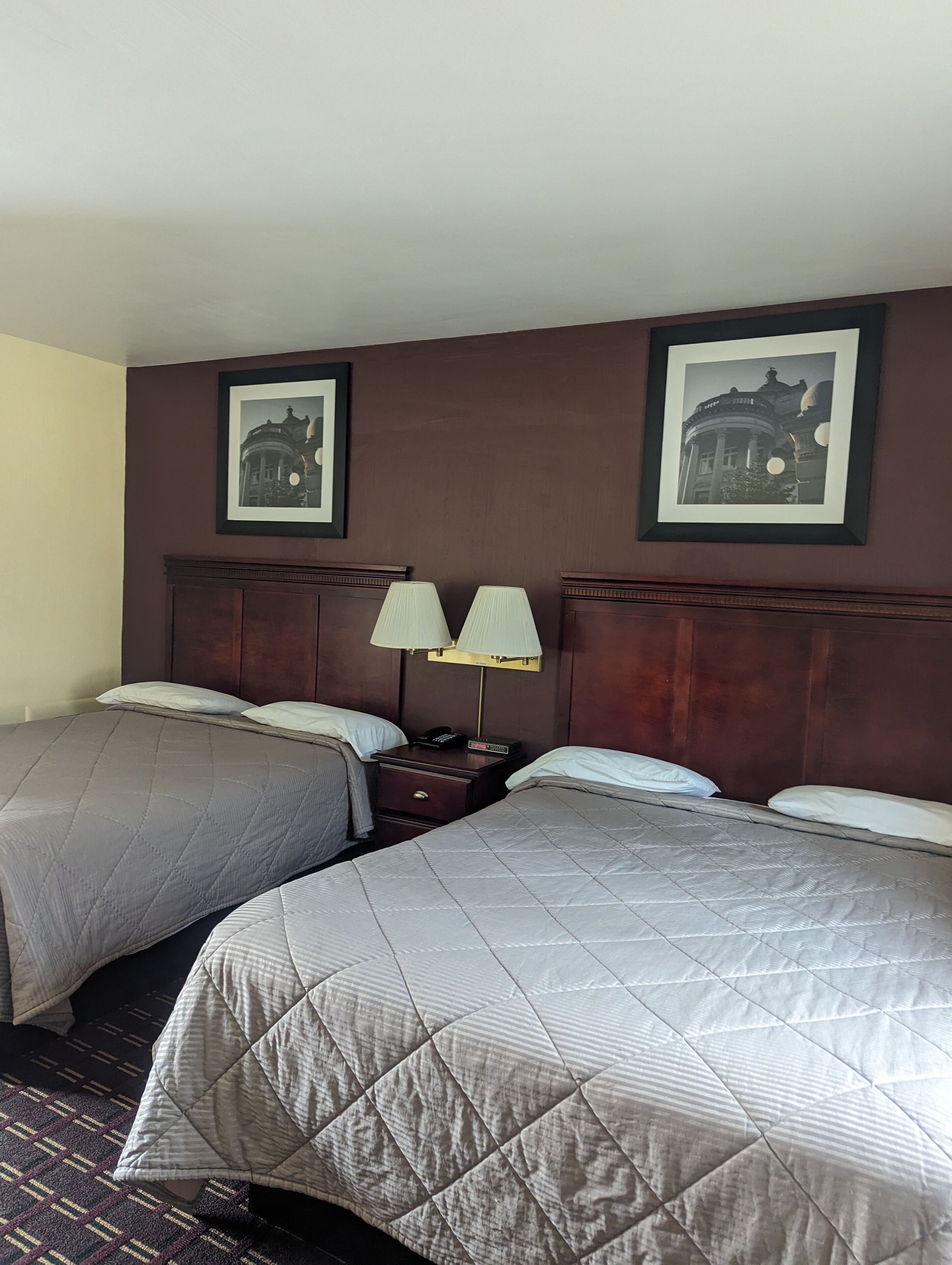 Una habitación de hotel con dos camas, una mesita de noche con lámparas y cuadros en la pared.