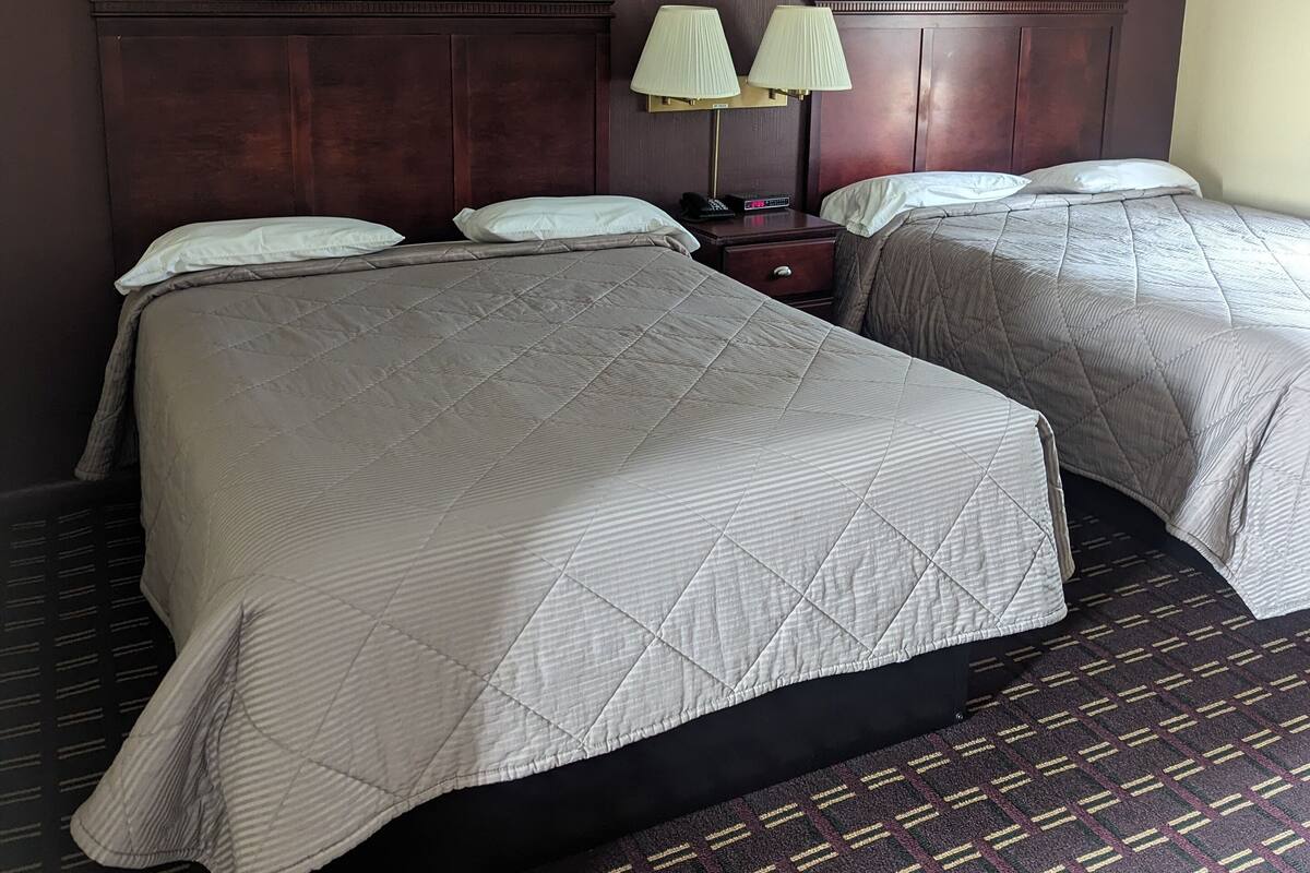 A hotel room with two beds, a nightstand, two lamps, and two framed pictures on the wall.
