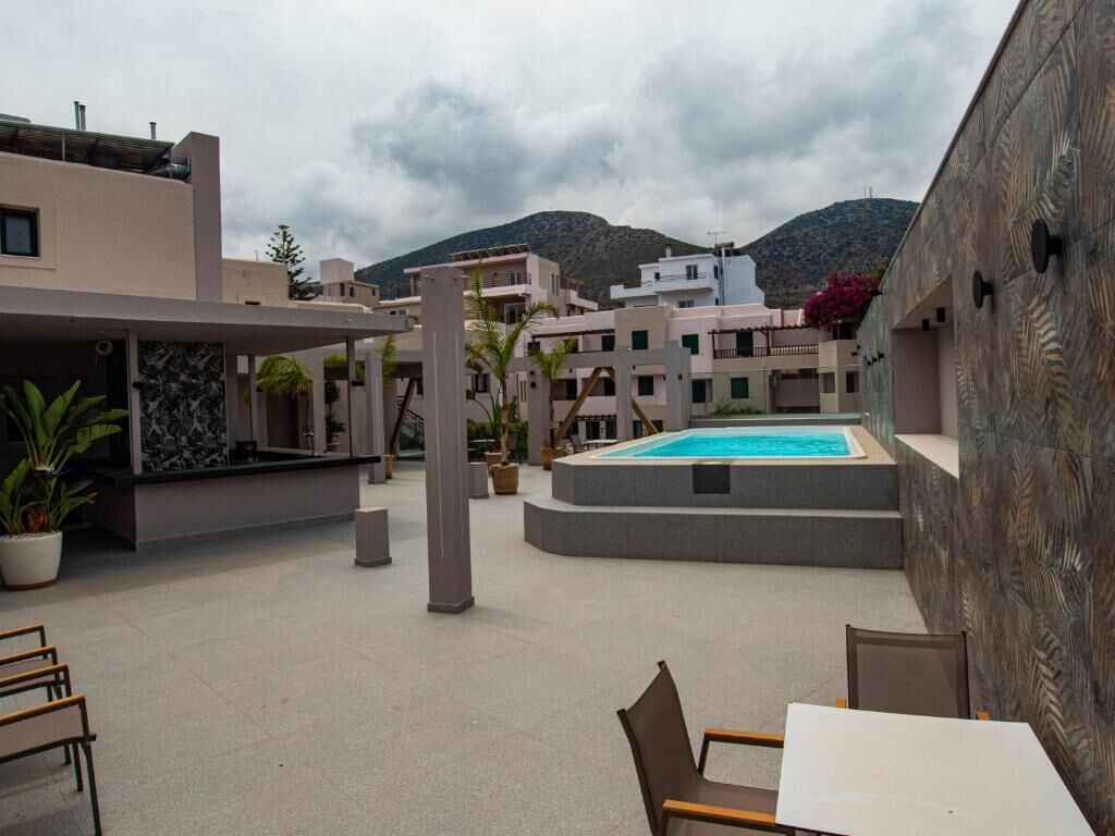 Un área de piscina al aire libre con piscina, asientos y edificios al fondo.