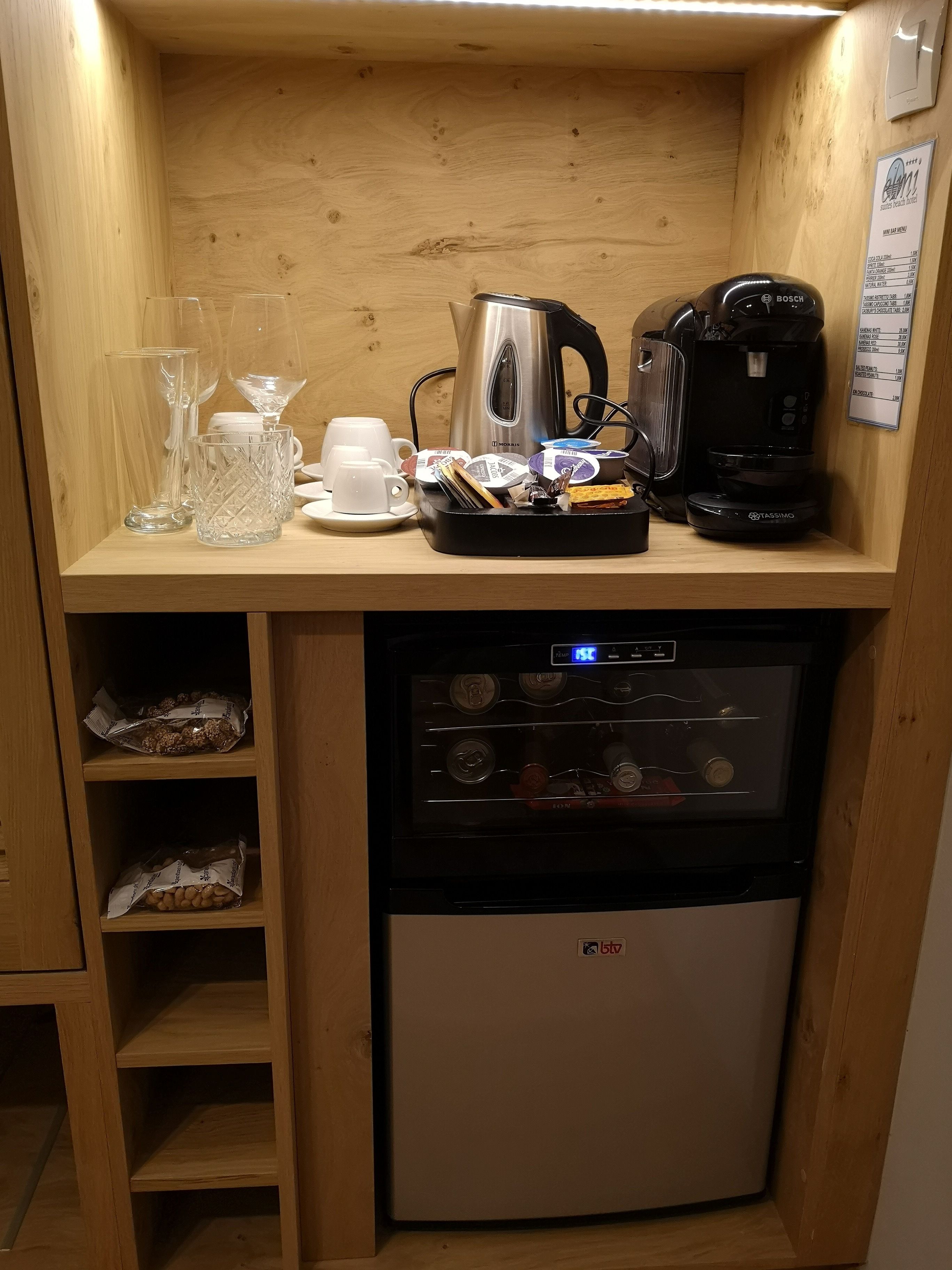 A compact kitchenette with a coffee maker, kettle, and storage shelves.