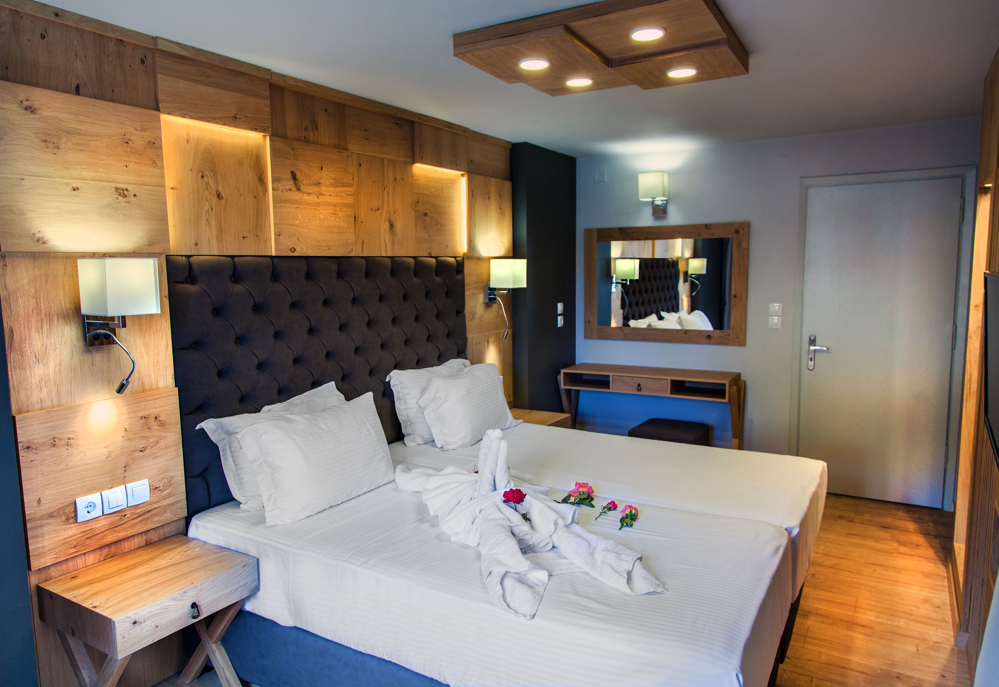Habitación de hotel con una cama grande, cabecera de madera, lámparas de noche, un espejo y una mesita de noche de madera.