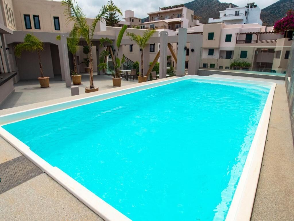 A rectangular swimming pool with a clear blue water surface, surrounded by a concrete deck and potted plants.