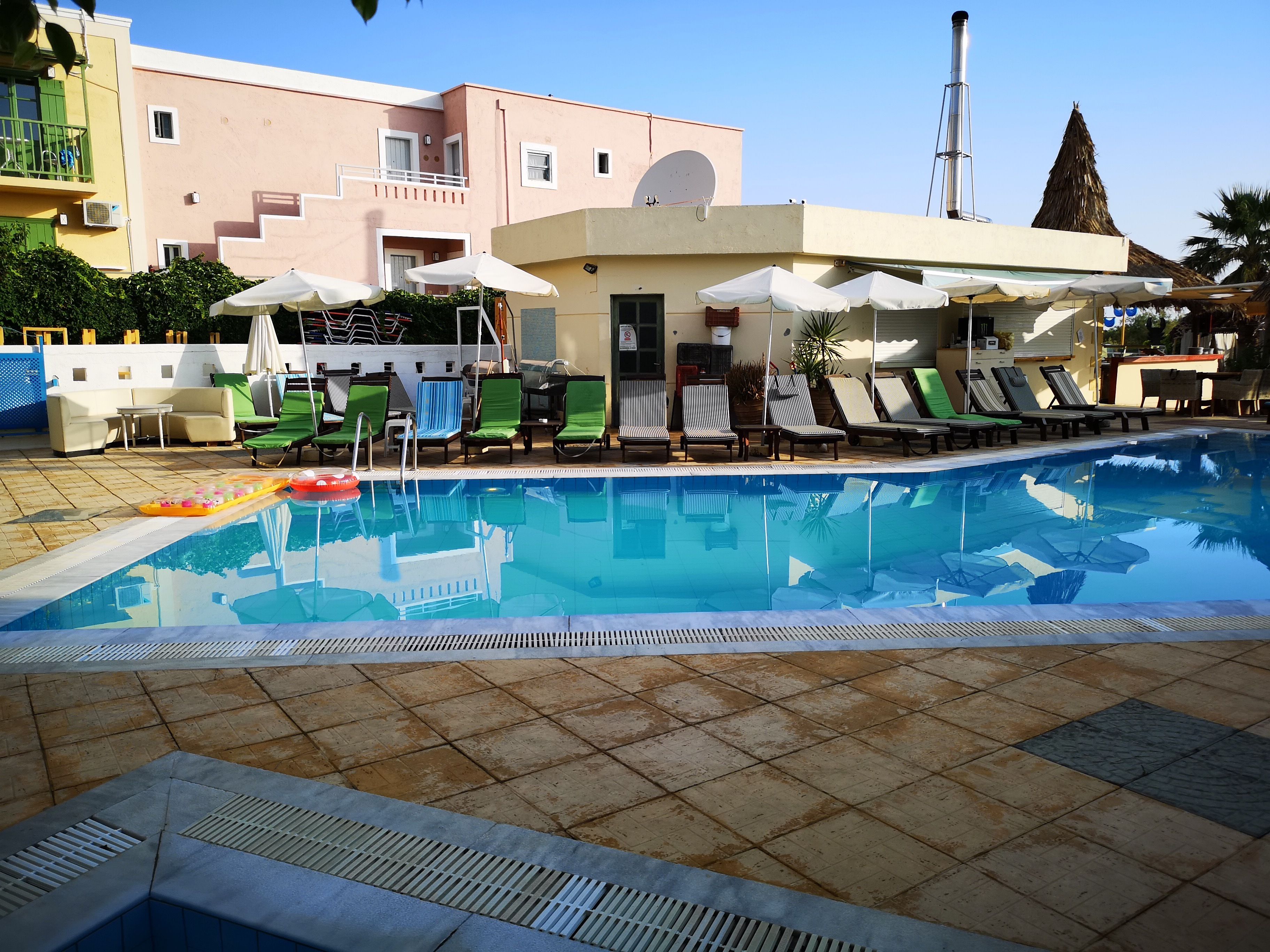 A swimming pool with lounge chairs and umbrellas, surrounded by buildings with balconies and a chimney.