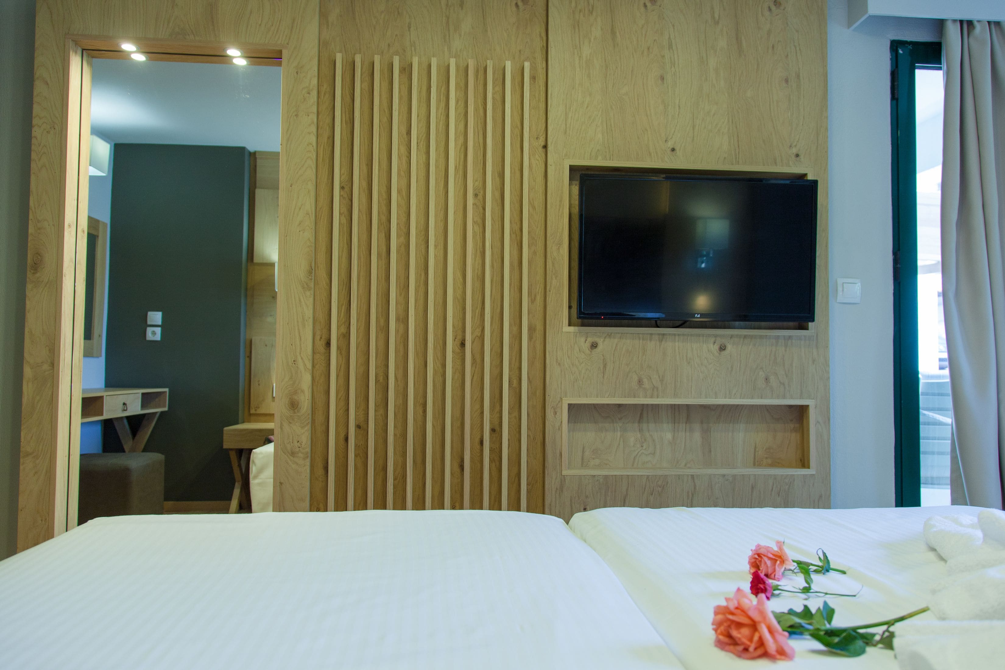 A hotel room with a bed, a TV mounted on the wall, a wooden panel wall, and a window with curtains.
