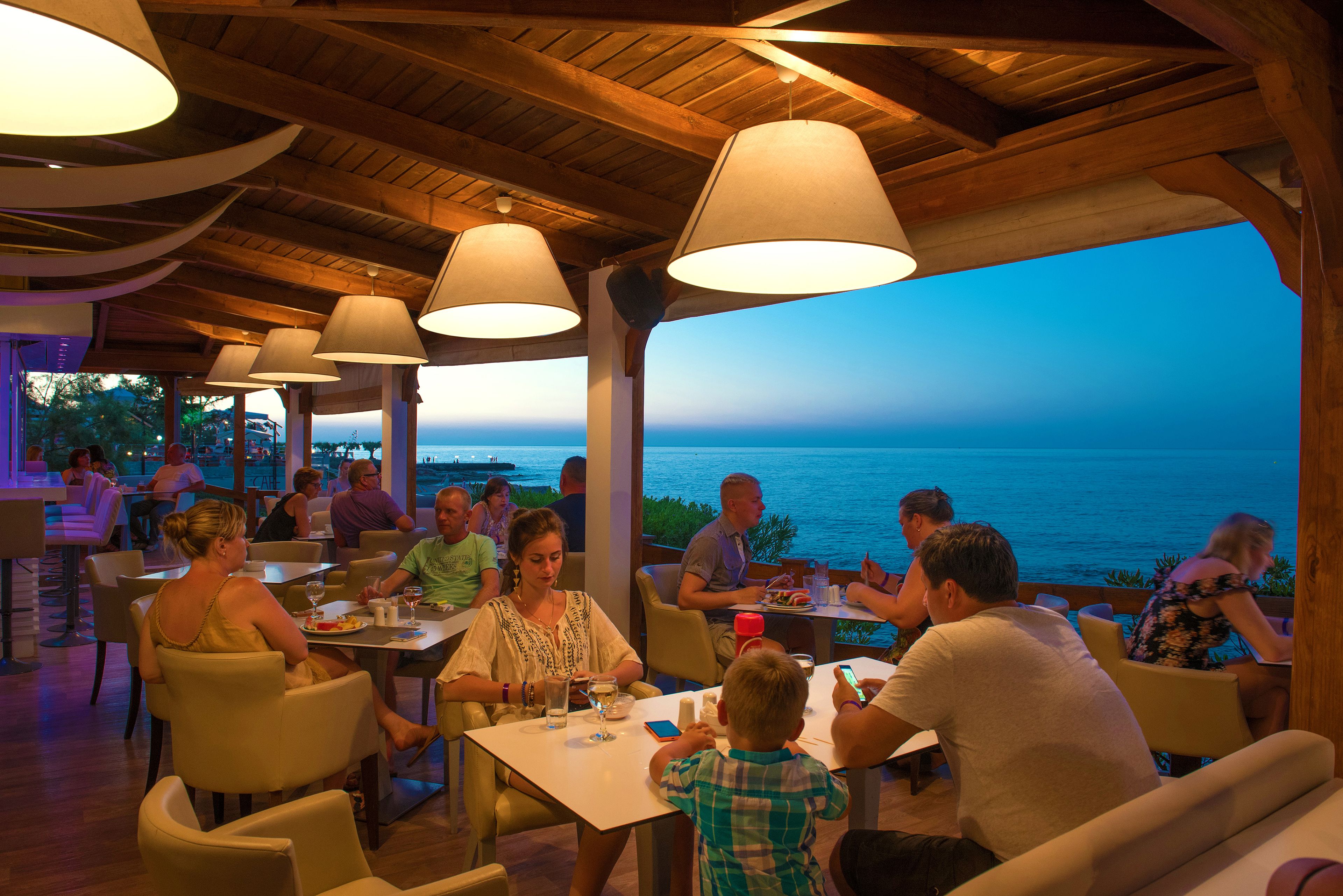An outdoor dining area with tables and chairs, overlooking a body of water.