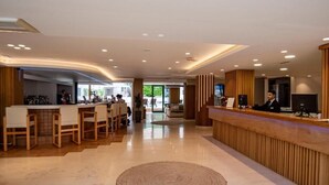 A modern hotel lobby with a reception desk, seating area, and a view into the dining space. - Elmi Suites Beach Hotel - All Inclusive (Hersonissos)