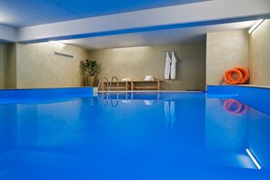 An indoor swimming pool with a clear blue water surface, a ladder, and a bench with towels. - Grand Hotel Palace (Ampelokipoi-Menemeni)