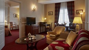 A hotel room with a living area featuring a sofa, a coffee table, a TV, and a dining table with chairs.