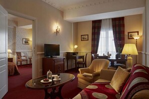 Une chambre d’hôtel dotée d’un espace salon comprenant un canapé, une table basse, un téléviseur et une table à manger avec des chaises.
