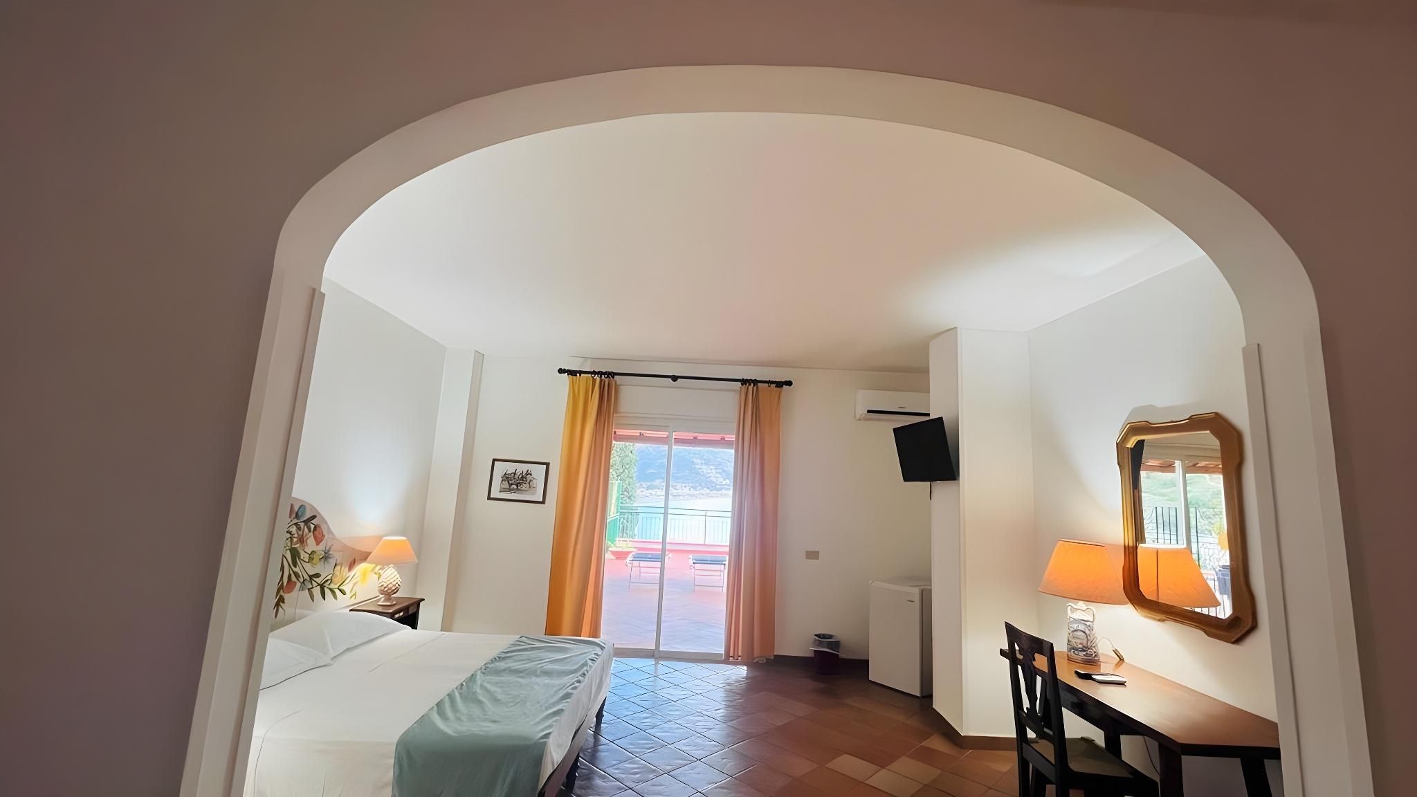 A hotel room with a bed, a desk, a chair, a TV, and a window with curtains.