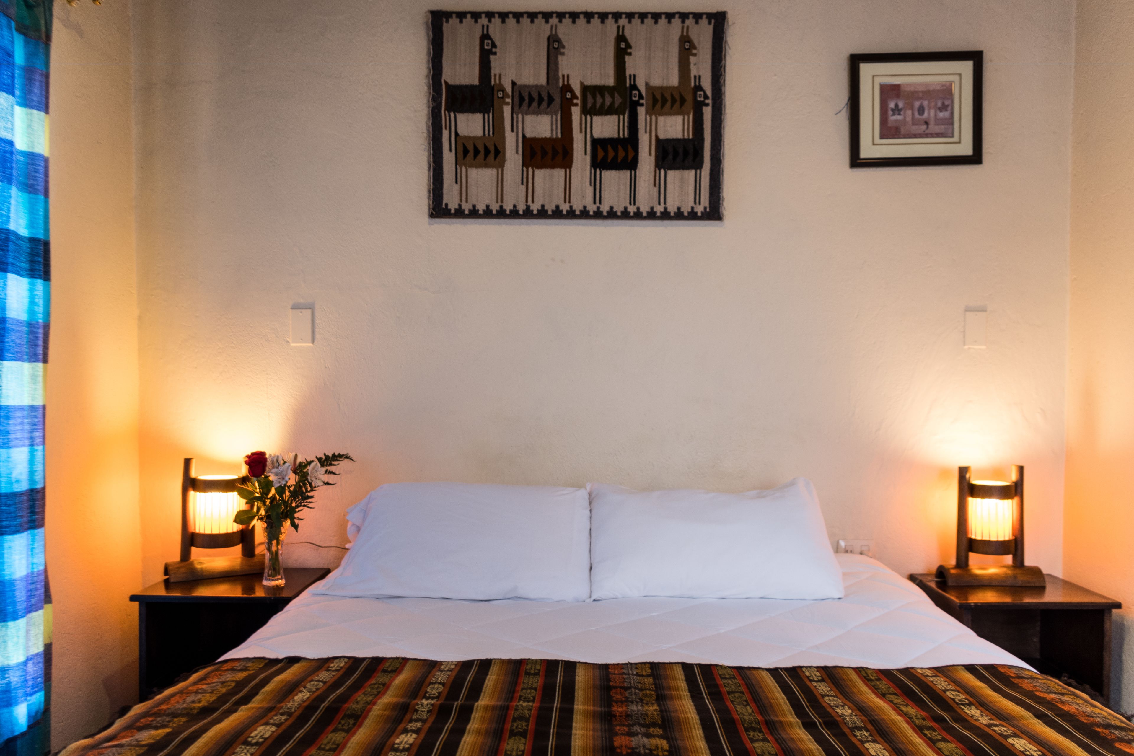 Une chambre d’hôtel comprenant un lit, deux tables de chevet avec des lampes, une œuvre d’art accrochée au mur et un tableau encadré.