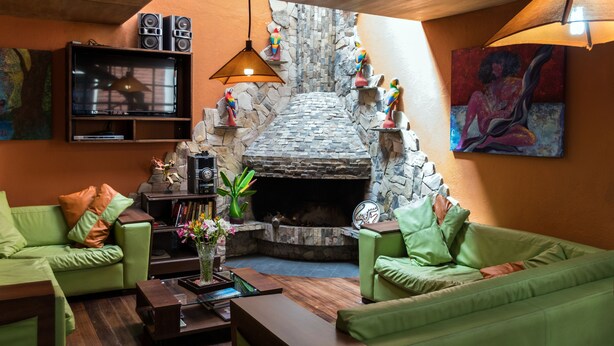 Ein Wohnzimmer mit Kamin aus Stein, grünen Sofas, einem Holztisch und einem Fernseher auf einer Ablagefläche.
