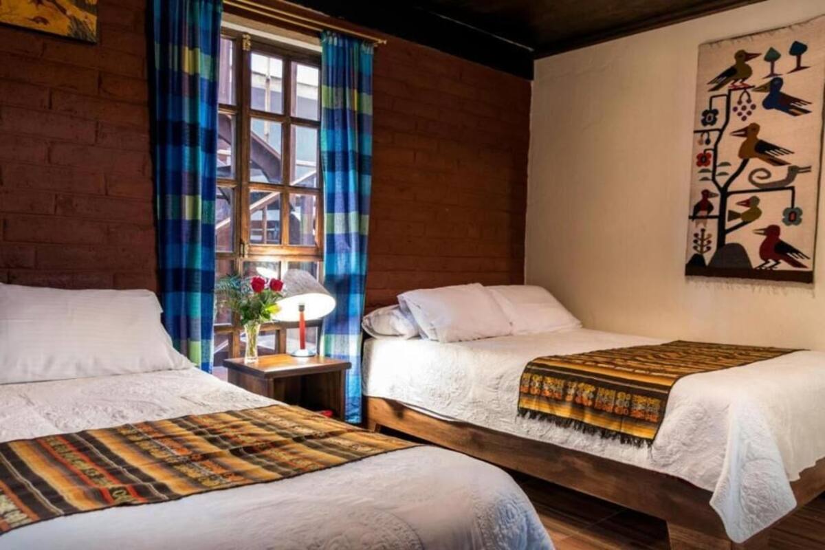 Une chambre avec deux lits, une fenêtre avec des rideaux bleus, une lampe sur une table de chevet et un tableau au mur.
