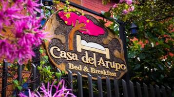 A sign for "Casa del Arupo Bed & Breakfast" with a bed illustration and a tree.