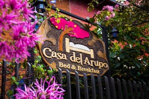 A sign for "Casa del Arupo Bed & Breakfast" with a bed illustration and a tree. - La Casa del Arupo (Quito)