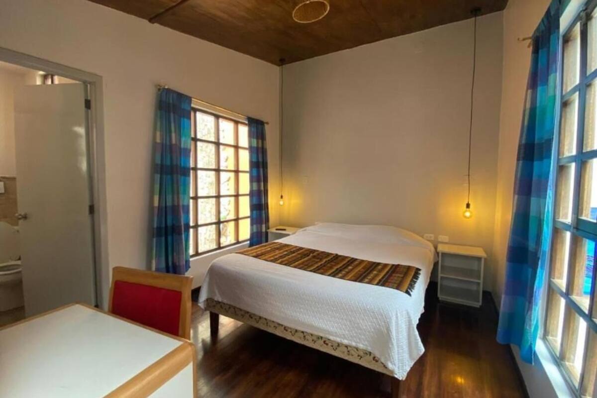 Une chambre à coucher avec un lit, une chaise, une table et une fenêtre avec des rideaux.