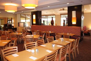 A restaurant with multiple tables and booths, wooden chairs, and a patterned wall. - Rosen Inn International (Orlando)
