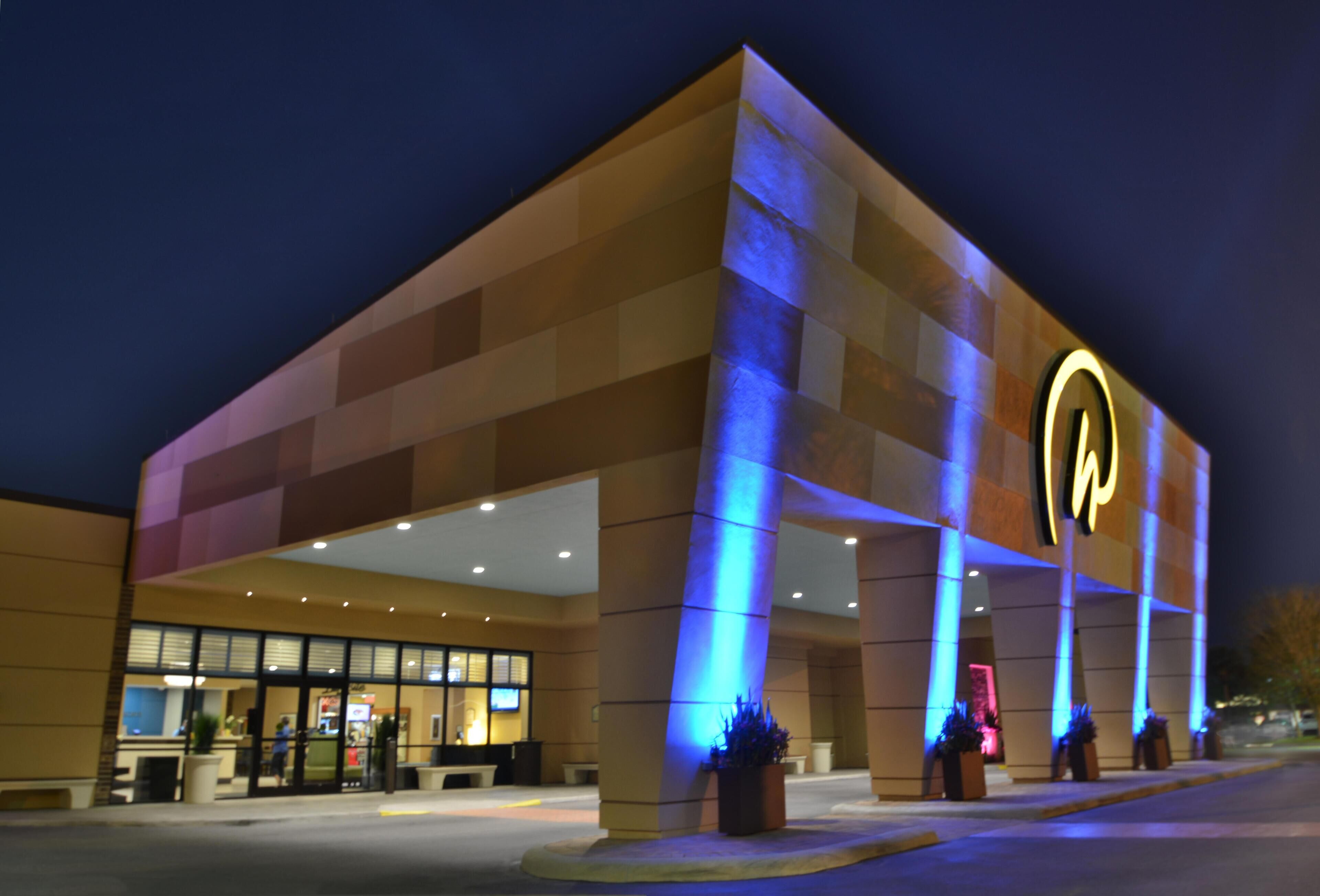 A hotel with a prominent illuminated logo, a covered entrance, and a well-lit facade.