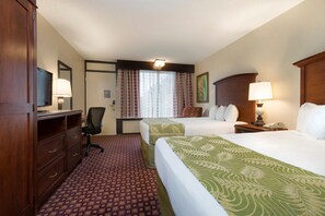 Quarto de hotel com cama, escrivaninha, cadeira e televisão.