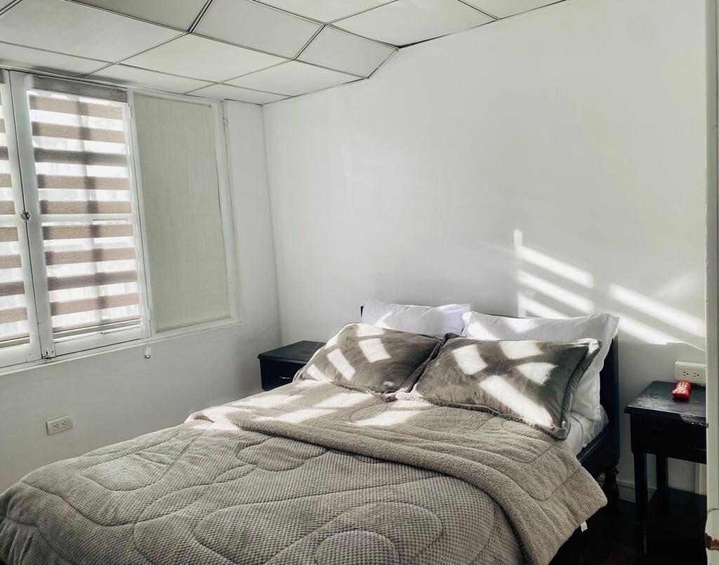 A bedroom with a bed, a nightstand, and a window with blinds.