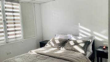A bedroom with a bed, a nightstand, and a window with blinds.