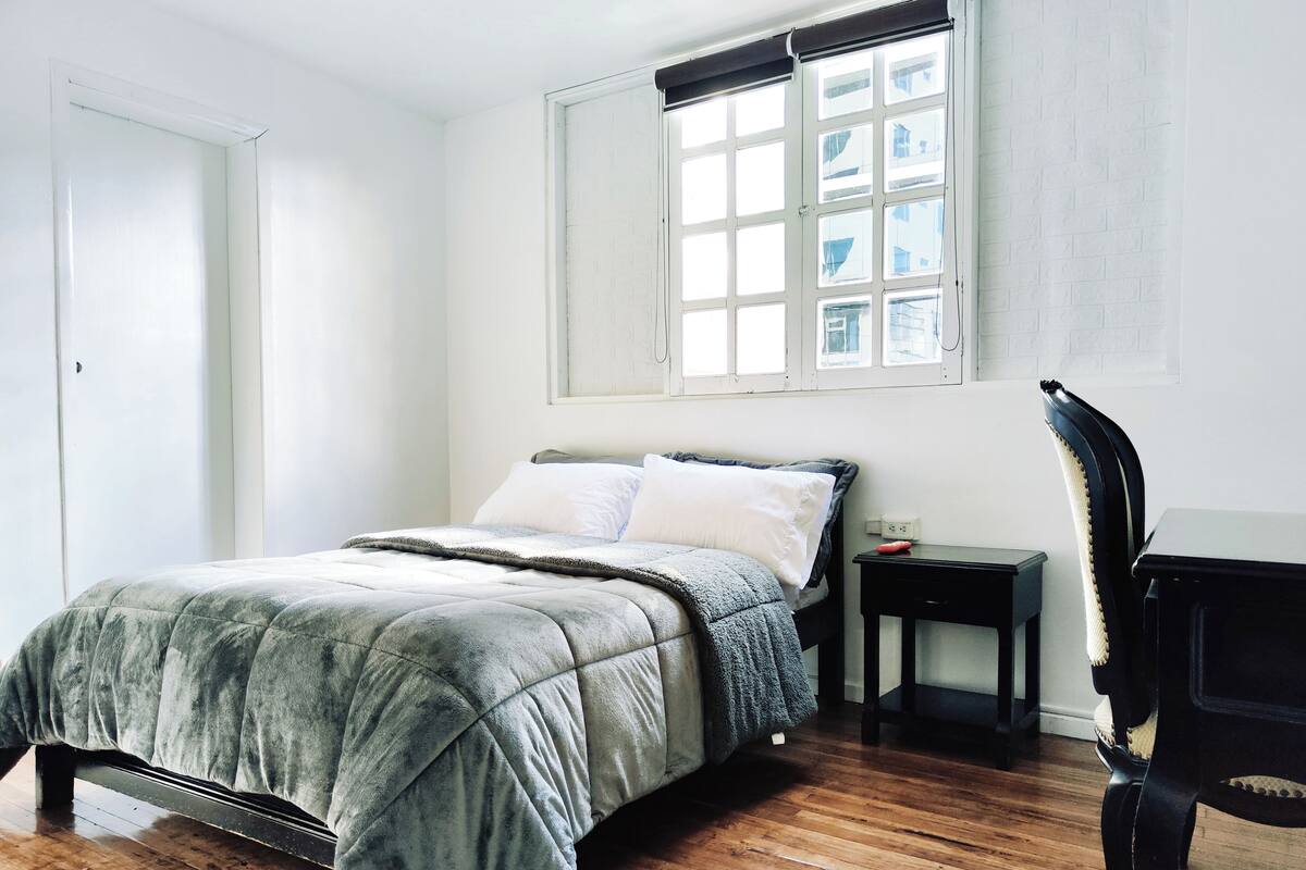 A bedroom with a bed, a chair, a nightstand, and a window.